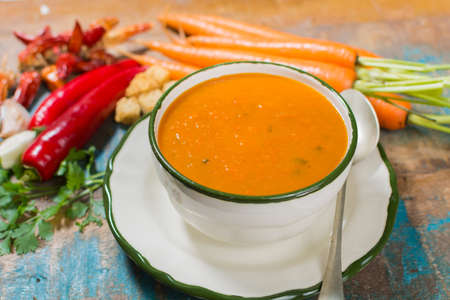 Spicy carrot soup with harissa made from hot chili pepper, lemon, garlic, coriander on blue wooden tableの写真素材