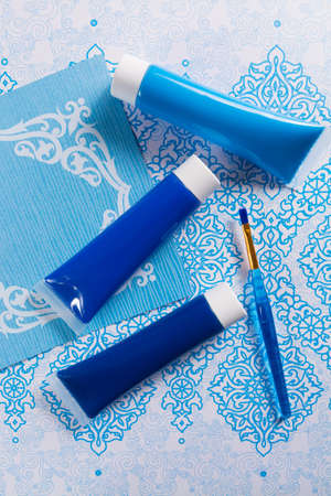 Blue, indigo, cobalt colours - home interieur design concept, on blue-white ornament, tubes with acrylic paint and blue brushの写真素材
