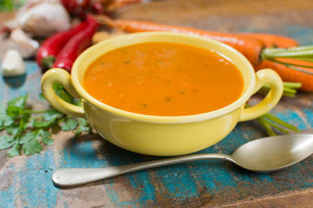 Spicy carrot soup with harissa made from hot chili pepper, lemon, garlic, coriander on blue wooden tableの写真素材