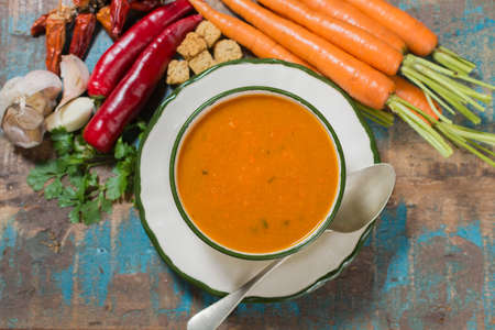 Spicy carrot soup with harissa made from hot chili pepper, lemon, garlic, coriander on blue wooden tableの写真素材
