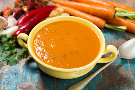 Spicy carrot soup with harissa made from hot chili pepper, lemon, garlic, coriander on blue wooden tableの写真素材