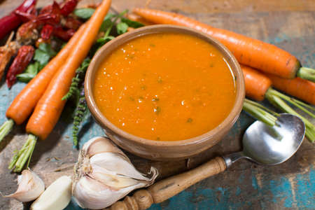 Spicy carrot soup with harissa made from hot chili pepper, lemon, garlic, coriander on blue wooden tableの写真素材