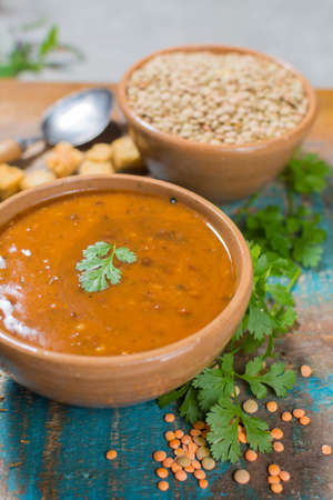 Homemade brown lentils soup in old clay bowl with green corianderの写真素材