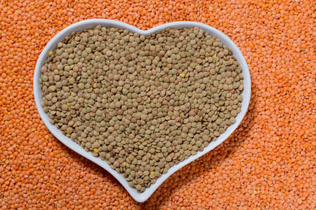 Heart form bowl with green lentils over red lentils background - healthy food conceptの写真素材