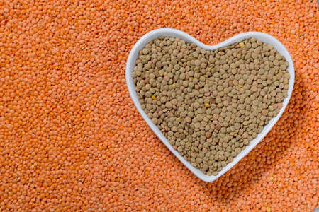 Heart form bowl with green lentils over red lentils background - healthy food conceptの写真素材