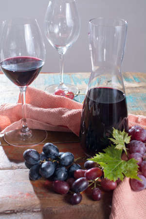 Small carafe with dry red wine, two wine glasses and grapes on the tableの写真素材