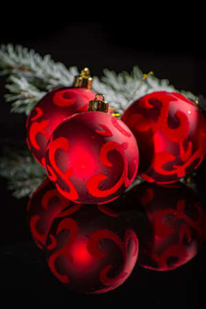 Red christmas tree decoration, red balls with ornament and green fir on black background with reflection close up copy spaceの写真素材