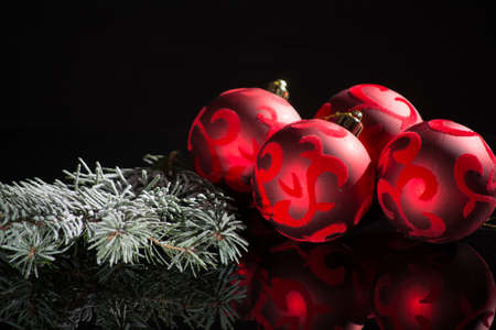 Red christmas tree decoration, red balls with ornament and green fir on black background with reflection close up copy spaceの写真素材
