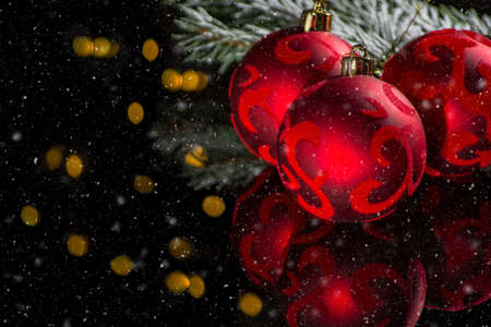 Red christmas tree decoration, red balls with ornament and green fir on black background with snow...