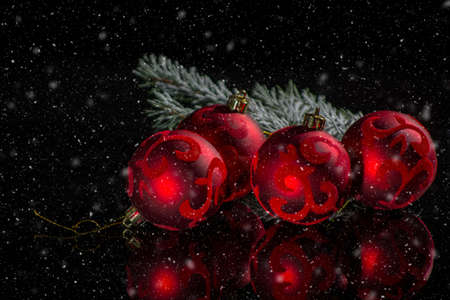 Red christmas tree decoration, red balls with ornament and green fir on black background with snow and reflection close up copy spaceの写真素材