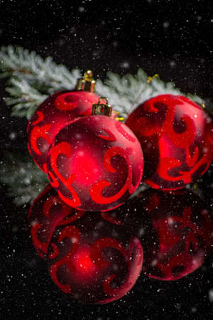 Red christmas tree decoration, red balls with ornament and green fir on black background with snow and reflection close up copy spaceの写真素材
