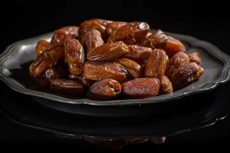 Sweet dessert dried palm date in old tin bowl, low key, dark theme, on black background with reflection copy spaceの写真素材