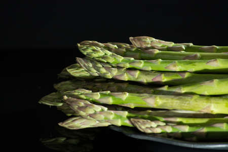 Fresh uncooked green asparagus on black background with reflection, low key, dark theme.の写真素材