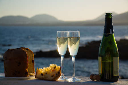 Sweet fruit Chrismas and New Year cake panettone with two glasses with champagne served outside with blue sea backgroundの写真素材