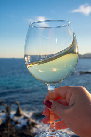 Tasting of glass of cold white wine served on outdoor terrace with beautiful romantic  sea view, woman handの写真素材
