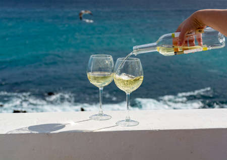 Waiter pouring glass of white wine on outdoor terrace with beautiful romantic  sea viewの写真素材