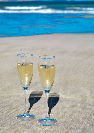 Two glasses of cold white champain or cava sparkling wine served on the white sandy tropical beach, luxury resort with sea view, romantic vacationの写真素材