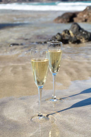 Two glasses of cold white champain or cava sparkling wine served on the white sandy tropical beach, luxury resort with sea view, romantic vacationの写真素材