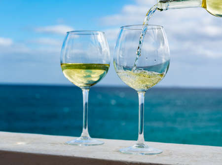 Waiter pouring glass of white wine on outdoor terrace with beautiful romantic  sea viewの写真素材