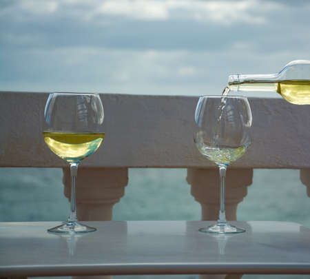Waiter pouring glass of white wine on outdoor terrace with beautiful romantic  sea viewの写真素材