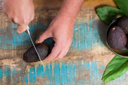 How to cut avocado, raw ripe dark green  avocados with leaves on wooden background top viewの写真素材