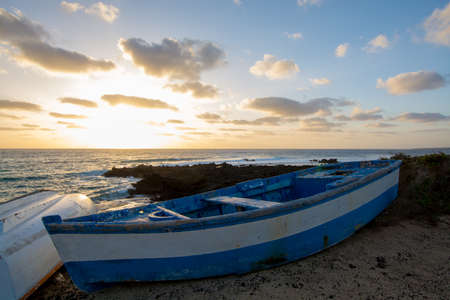 Sunset over the sea landscape with old blue wooden fishing boat