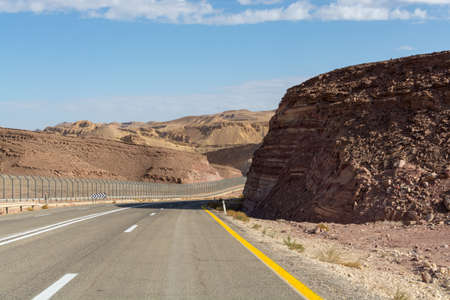 Asphalt road in desert Negev, Israel, road 12, transport infrastructure in desert, view on fence wall on boarder with Egypt, scenic mountains route from Eilat to north of Israelの写真素材