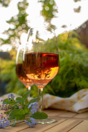 Two cold rose wine glasses served on outdoor terrace in garden with flowers in sunny dayの写真素材