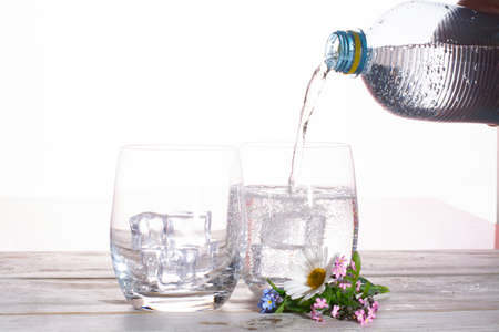 Pouring of sparkling soda mineral drink water in glasses with ice cubes close up copy space