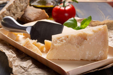 Traditional italian food - aged Italian parmesan hard cheese Parmigiano-Reggiano with cheese knife, tomato, basil, olive oilの写真素材