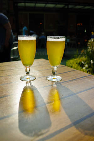 Two cold light unfiltered beer in glasses served on sunny outdoor terrace in gardenの写真素材
