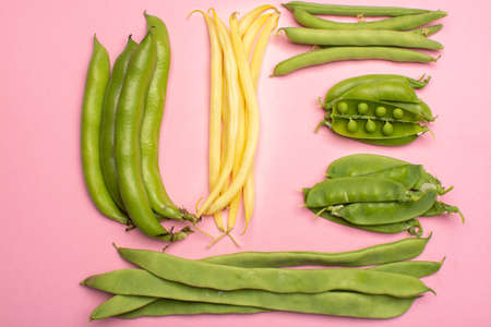 Flat lay food concept with fresh legumes,  green ripe bread beans, garden beans, sugar snaps, sweet peas, peas and yellow butter beans copy space close up isolated on pink backgroundの写真素材