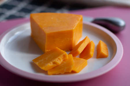 Triangle piece of British hard cow  dark yellow cheddar cheese on pink table close upの写真素材