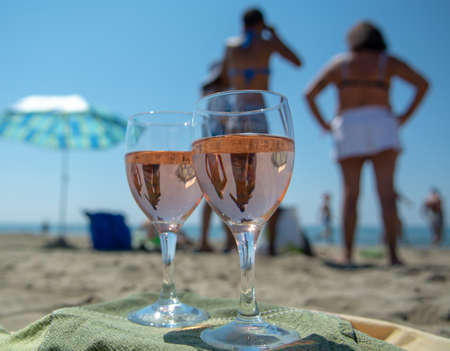 beach party with sea view, romantic celebration on sunny sandy beach, two glasses with rose wine close upの写真素材