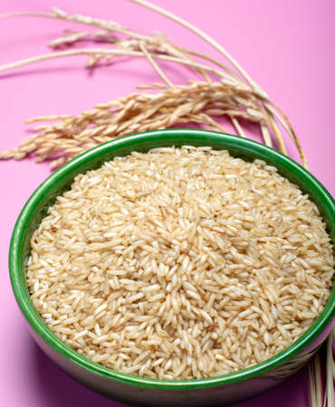 Bowl with organic brown uncooked rice and dried rice plant on pink background close upの写真素材