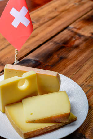 Assortment of Swiss cheeses Emmental or Emmentaler medium-hard cheese with round holes, Gruyere, appenzeller and raclette used for traditional cheese fondue and gratin and flag of Switzerlandの写真素材