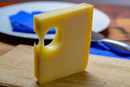 Block of Swiss Emmental or Emmentaler medium-hard cheese with round holes made from cow milk in...