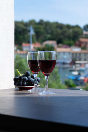Two wine glasses with red wine served with red grape on outdoor terrace in sunny summer dayの写真素材
