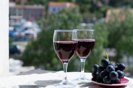 Two wine glasses with red wine served with red grape on outdoor terrace in sunny summer dayの写真素材