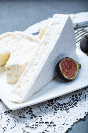 Two pieces of French soft cheeses Brie and Camembert with white mold and strong odor, served with...