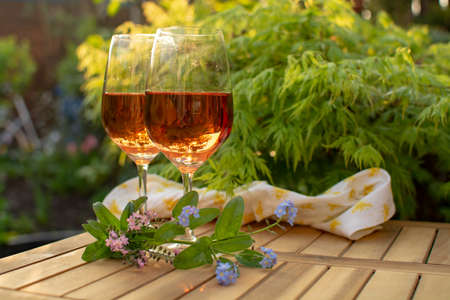 Two cold rose wine glasses served on outdoor terrace in garden with flowers in sunny dayの写真素材