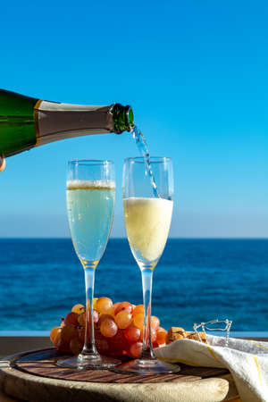 Waiter pouring Champagne, prosecco or cava in two glasses on outside terrace with sea view  close upの写真素材