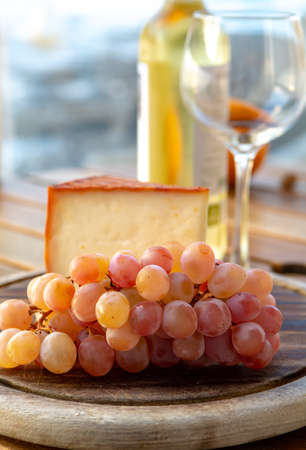 Spanish goat milk cheese with paprika coating and ripe pink table grapes served with white wine on outdoor terrace close upの写真素材