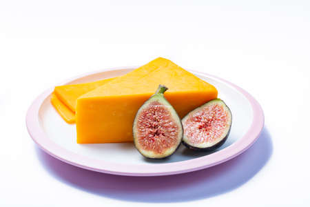 Piece of hard orange Cheddar cheese and fresh ripe figs on white board isolated, close up