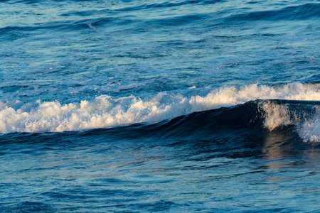 Background with dark blue ocean water waves close up on sunset