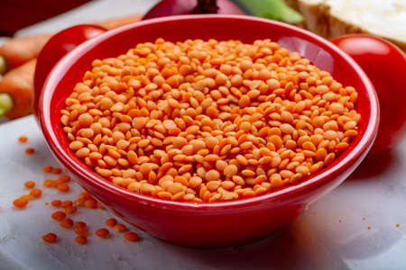 Dried orange lentils legume in red bowl close up
