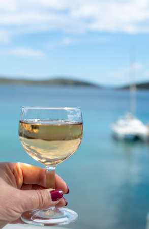 hand with glass of white wine served outside on balcony with sea view close up