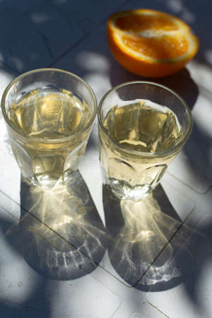 White wine served outside in garden on white table with fresh orange in sun lights close up