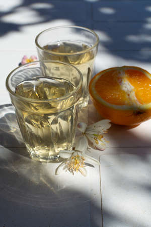 White wine served outside in garden on white table with fresh orange in sun lights close up
