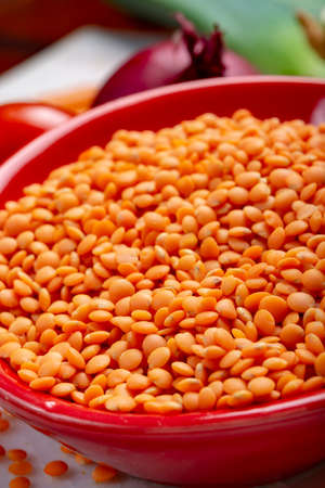 Dried orange lentils legume in red bowl close up
